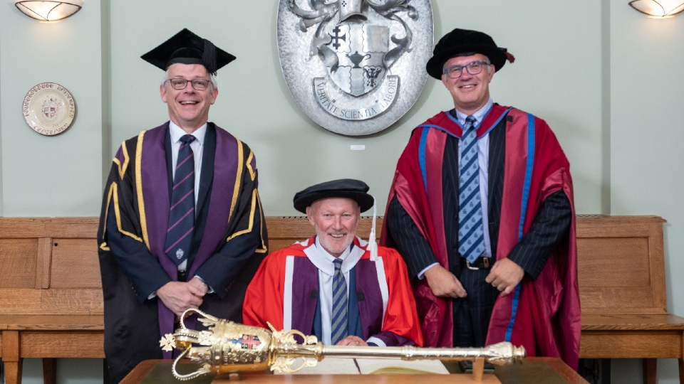 Commodore David Pond, seated in the centre, with Provost and Deputy Vice-Chancellor Professor Chris Linton (left), and Professor Mark Lewis, Dean of School of Sport, Exercise and Health Sciences (right). They all wear robes. 